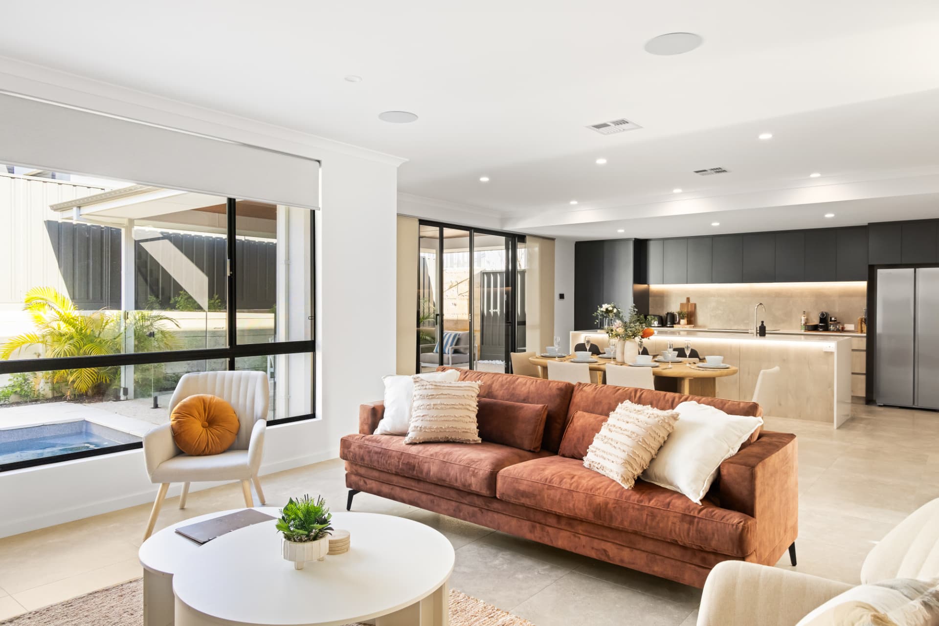 Open-plan living room with rust velvet sofa, kitchen and pool beyond